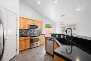Kitchen featuring lofted ceiling, appliances with stainless steel finishes, tasteful backsplash, decorative light fixtures, and recessed lighting