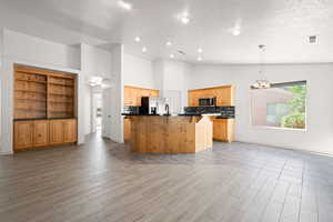 Kitchen featuring a textured ceiling, a center island with sink, light wood-type flooring, decorative light fixtures, and stainless steel appliances