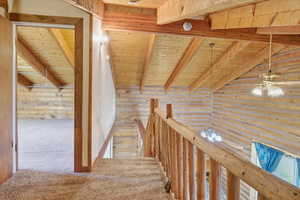 Hallway featuring rustic walls, a wooden ceiling with exposed beams, carpet flooring, and an upstairs landing