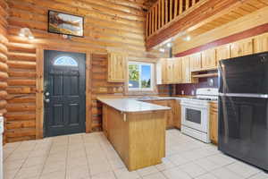 Kitchen featuring freestanding refrigerator, light countertops, a peninsula, white range with gas cooktop, and rustic walls