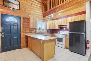 Kitchen with light countertops, freestanding refrigerator, white gas range, log walls, and a peninsula