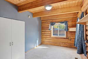 Unfurnished bedroom featuring rustic walls, carpet flooring, a wood ceiling with exposed beams, and a closet