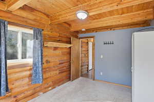 Unfurnished bedroom with rustic walls, carpet flooring, and a wood ceiling with exposed beams