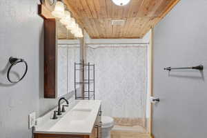 Full bathroom with a textured wall, wooden ceiling, vanity, and shower / tub combo with curtain
