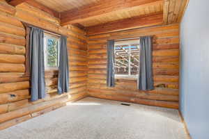 Empty room featuring carpet floors, a wooden ceiling with exposed beams, and rustic walls