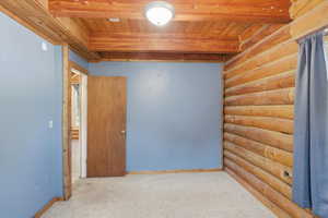 Unfurnished room featuring rustic walls, carpet floors, and a wooden ceiling with exposed beams