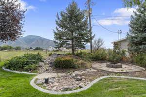 View of green lawn with a fire pit, a patio, a mountain view, and a rural view