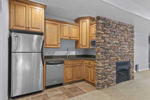 Kitchen featuring appliances with stainless steel finishes, dark stone countertops, light carpet, light stone finish flooring, and a fireplace