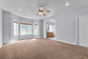 Unfurnished bedroom with a textured ceiling, light carpet, connected bathroom, a ceiling fan, and arched walkways