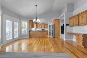 Kitchen with tasteful backsplash, light wood-style floors, pendant lighting, lofted ceiling, and a chandelier