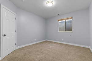 Empty room with light carpet and a textured ceiling