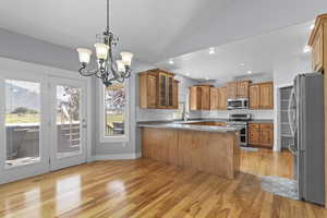 Kitchen featuring stainless steel appliances, hanging light fixtures, a peninsula, a chandelier, and lofted ceiling