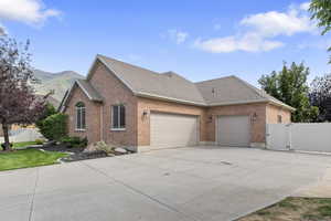 View of side of property with a shingled roof, brick siding, driveway, a garage, and a gate