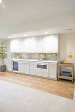 Bar featuring white cabinets, light countertops, light wood-type flooring, tasteful backsplash, and recessed lighting