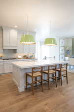 Kitchen with a kitchen breakfast bar, light wood-style floors, white cabinets, an island with sink, and decorative backsplash