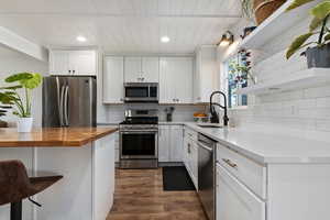 Kitchen featuring wood counters, open shelves, appliances with stainless steel finishes, white cabinetry, and dark wood-type flooring