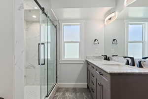 Full bath featuring double vanity, a marble finish shower, and dark marble finish flooring