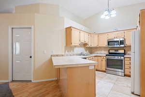 Kitchen featuring light brown cabinets, appliances with stainless steel finishes, a peninsula, decorative backsplash, and a breakfast bar
