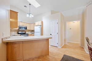 Kitchen featuring a peninsula, a skylight, stainless steel appliances, light wood-style floors, and a chandelier