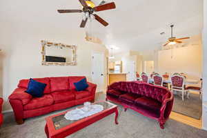 Living room featuring vaulted ceiling, a ceiling fan, and carpet floors