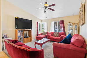 Living room with a ceiling fan, a textured ceiling, carpet floors, and lofted ceiling