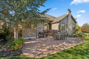 Back of house featuring a patio, stone siding, a chimney, and roof with shingles