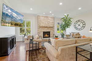 Living area with hardwood floors, crown molding, stone fireplace, arched walkways, recessed lighting, and a chandelier