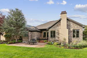 Back of house with a patio, a lawn, a chimney, and stone siding