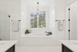 Master bathroom with double vanities, marble countertops, floors and shower, a garden tub, chandelier, and crown molding