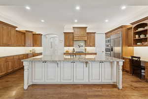 Kitchen featuring solid wood cabinets and floors, pot filler, open shelving, granite countertops, decorative backsplash, and crown molding,