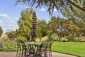 Deck featuring outdoor dining area, a yard, and view of scattered trees