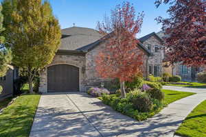 French provincial home with stone siding, driveway, and 3 car attached garage