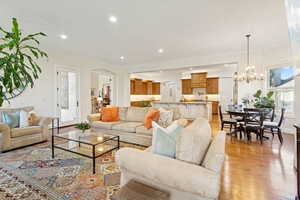 Living area with hardwood floors, crown molding, stone fireplace, arched walkways, recessed lighting, and a chandelier