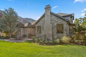 Back of property featuring a lawn, stone siding, and a patio