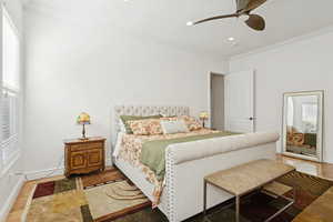 Master bedroom on main level with ornamental molding, wood finished floors, crown molding, ceiling fan, and recessed lighting
