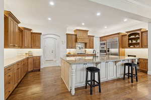 Kitchen featuring solid wood cabinets and floors, pot filler, open shelving, granite countertops, decorative backsplash, and crown molding,