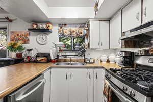 Kitchen featuring stainless steel appliances, white cabinetry, light countertops, and under cabinet range hood