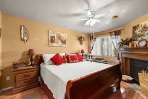Bedroom with a fireplace with flush hearth, light wood-style flooring, a textured ceiling, and ceiling fan
