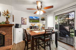 Dining space featuring light wood-style flooring, ceiling fan, and a brick fireplace