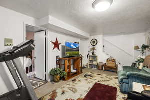 Living area with a textured ceiling, carpet flooring, and stairs