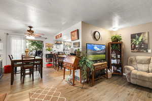 Living room with a textured ceiling, light wood-style flooring, and ceiling fan