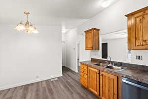 Kitchen featuring dark countertops, stainless steel dishwasher, dark wood-style flooring, a chandelier, and brown cabinets