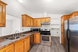 Kitchen with stainless steel appliances, light wood-type flooring, lofted ceiling, dark countertops, and under cabinet range hood