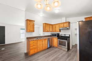 Kitchen featuring appliances with stainless steel finishes, light wood finished floors, brown cabinetry, a chandelier, and dark countertops