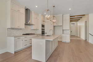Kitchen featuring tasteful backsplash, wall chimney exhaust hood, hanging light fixtures, a chandelier, and light wood finished floors