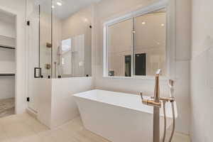Bathroom with a freestanding bath, a shower stall, tile patterned flooring, a walk in closet, and tile walls