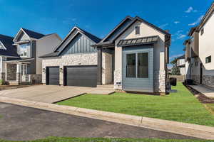 View of front facade featuring stone siding, a standing seam roof, a front lawn, and driveway