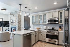 Kitchen with open floor plan, high quality appliances, a peninsula, pendant lighting, and a stone fireplace