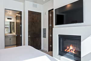 Bedroom featuring a glass covered fireplace, light carpet, electric panel, and ensuite bathroom