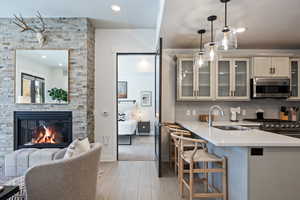 Kitchen featuring light wood finished floors, glass insert cabinets, a breakfast bar, pendant lighting, and appliances with stainless steel finishes